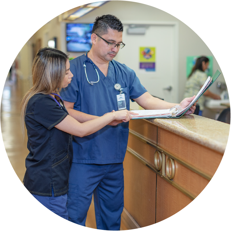 Male nurse speaks to female nurse near a nurse's stand